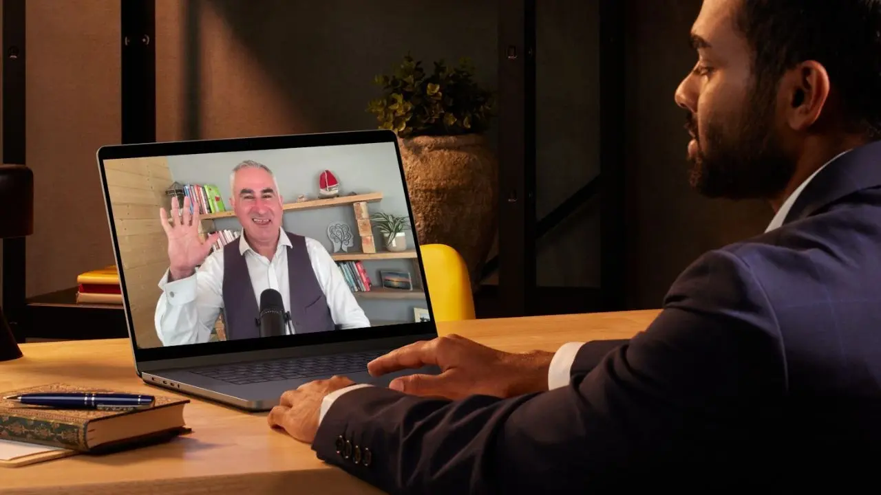Laptop showing a video conference call on a wooden desk next to a teal mug